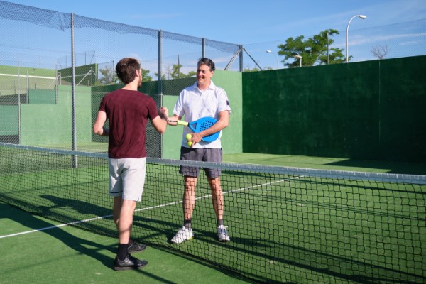 Dos jugadores de pádel masculinos sonriéndose y dándose las manos después de un partido en una cancha de pádel al aire libre